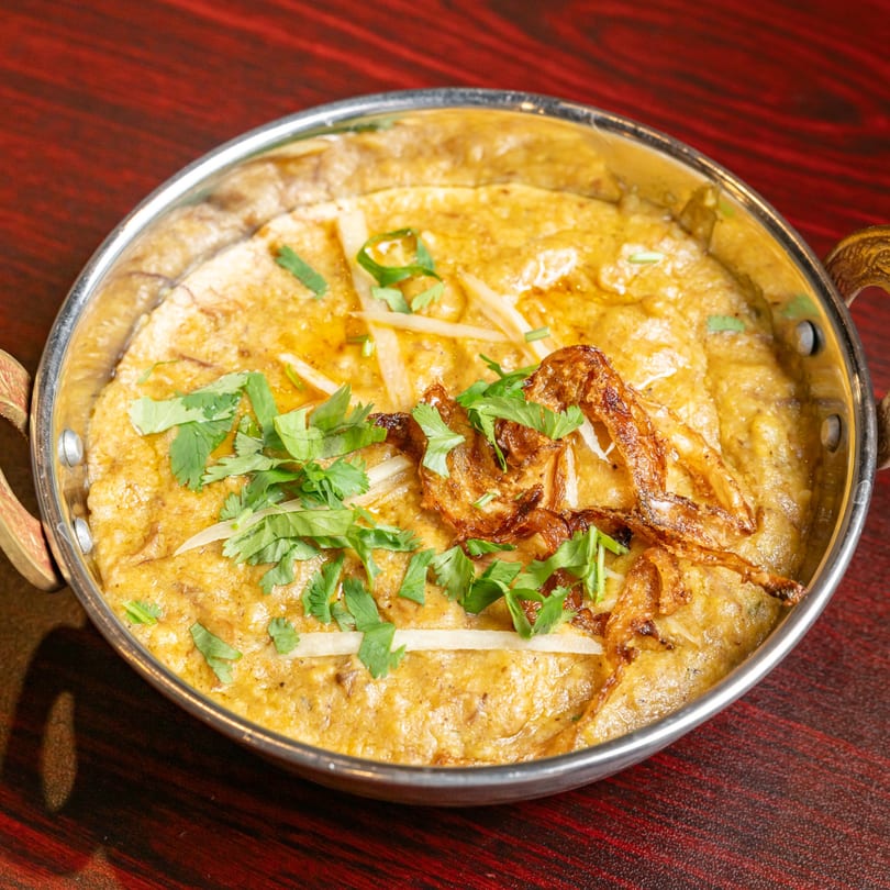 Indian Haleem, a thick stew, garnished with cilantro, ginger, and fried onions in a metal bowl.