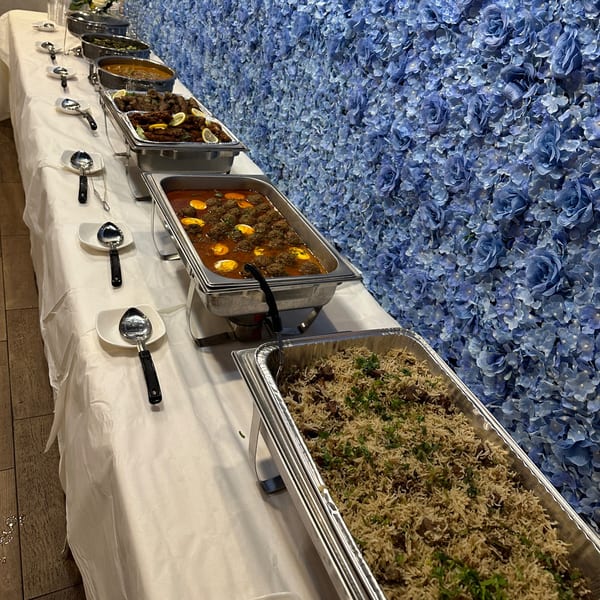 A buffet line of Indian dishes, including rice, curries, and kabobs, against a blue floral wall.