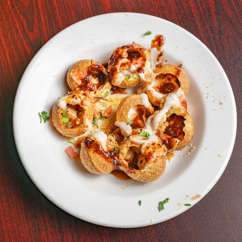 A white plate holds several Indian pani puri, filled with sauce, yogurt, and toppings.