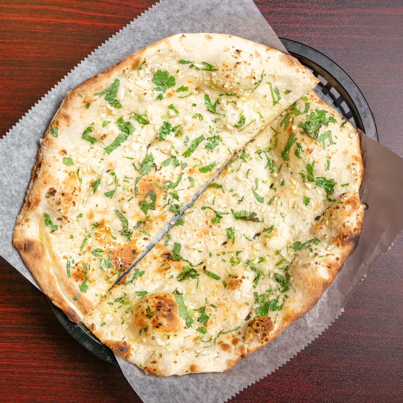 Garlic naan bread, garnished with fresh cilantro, served in a black basket on a wooden table.