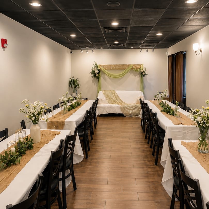 A long, narrow event room with two rows of tables set for a banquet, leading to a decorated sofa.