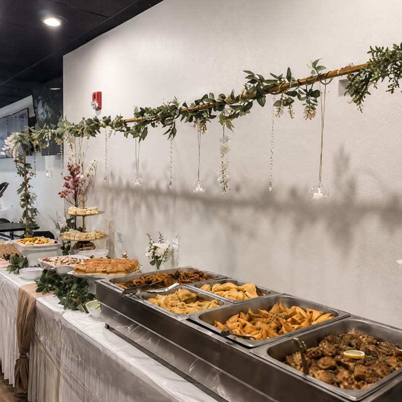 Buffet table with chafing dishes of food, desserts, and decorative greenery with hanging candles.