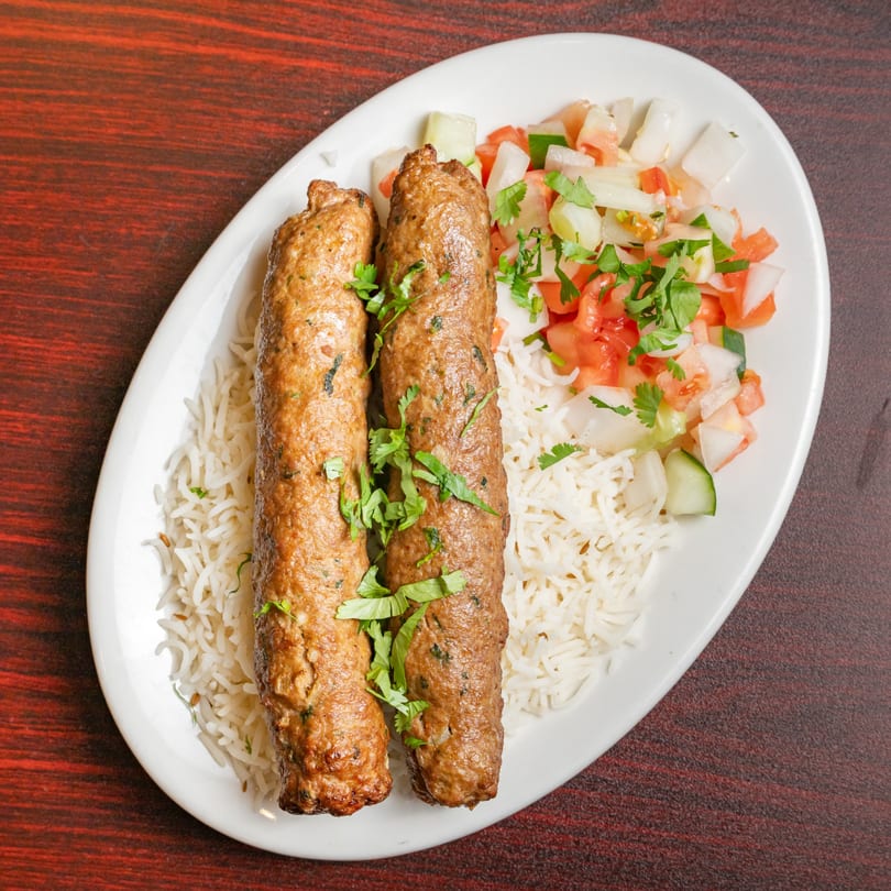 Two Indian seekh kabobs with white rice and a side salad on a white plate.